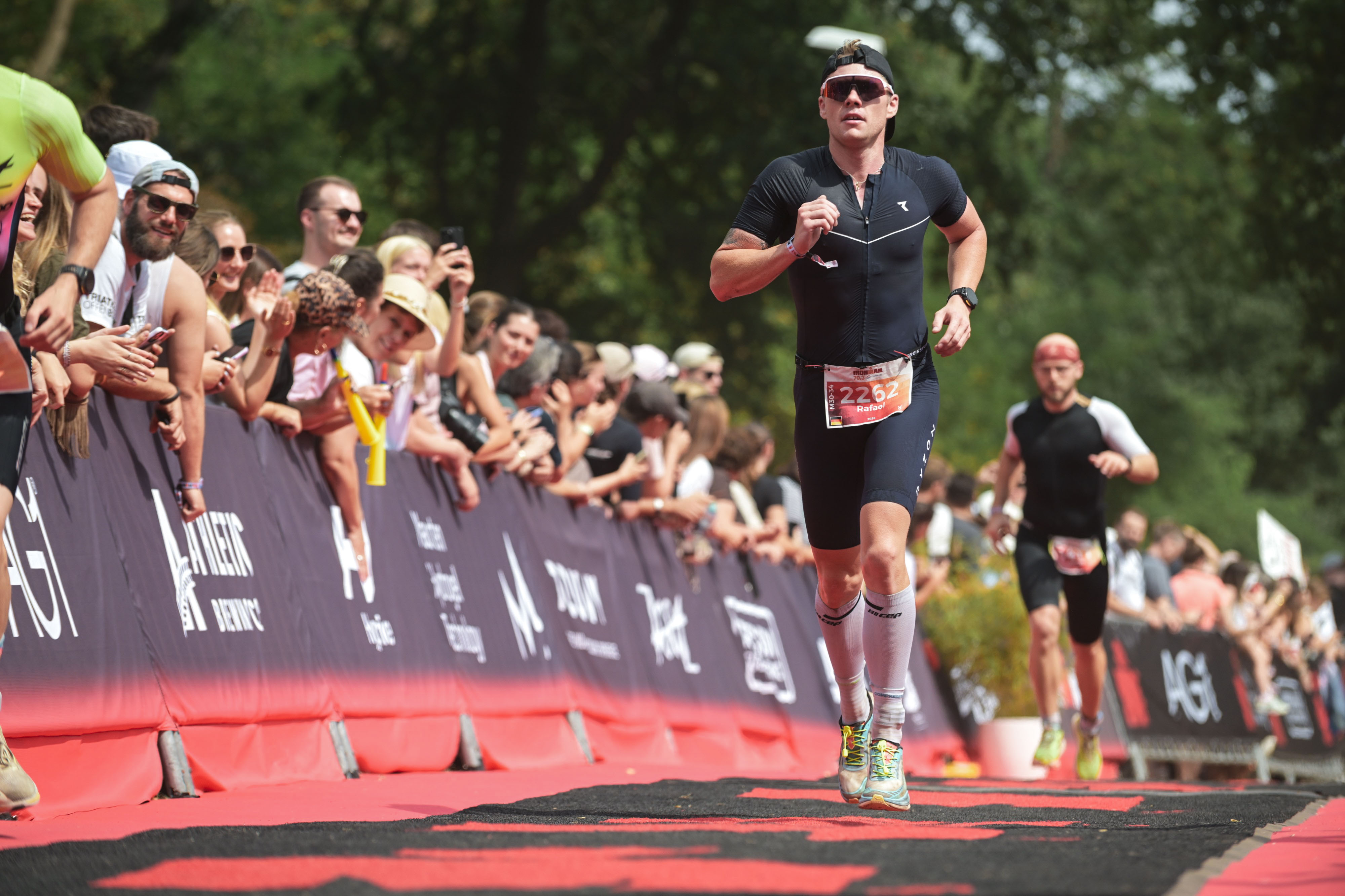Disziplin Laufen - Iron Man 16.0.2026 Mann in Sportkleidung läuft bei einem Wettkampf an einer Absperrung mit jubelnden Zuschauern vorbei