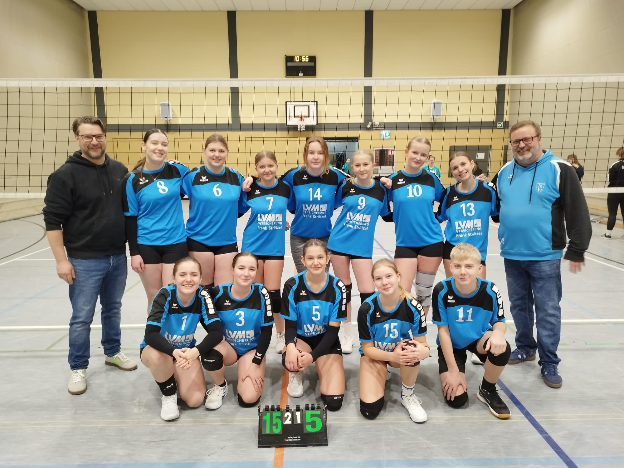 Volleyball U16 beim Auswärtsspiel in Belm am 08.02.2026 Das Bild zeigt ein Gruppenfoto einer Jugend-Volleyballmannschaft in einer Sporthalle. Szene & Umgebung: Die Aufnahme wurde in einer typischen Schulsporthalle gemacht. Im Hintergrund ist ein Volleyballnetz, eine Basketballkorb-Anlage und eine digitale Hallenuhr (10:56 Uhr) zu sehen. Der Hallenboden ist mit Spielfeldmarkierungen versehen. Personen: In der Mitte steht eine Mannschaft aus jugendlichen Spielerinnen (U16), die blaue Trikots mit schwarzen Akzenten tragen. Die Trikots haben Rückennummern (z. B. 8, 6, 7, 14, 9, 10, 13, 1, 3, 5, 15, 11) und einen Sponsor-Aufdruck. Einige Spielerinnen stehen in der hinteren Reihe, andere knien vorne. Links und rechts außen stehen zwei erwachsene Männer, vermutlich Trainer oder Betreuer. Alle blicken in die Kamera und lächeln – die Stimmung wirkt zufrieden und stolz. Besonderes Detail: Vor der Mannschaft steht eine kleine Anzeigetafel mit dem Ergebnis: 15 : 5 In der Mitte ist zusätzlich eine „2“ zu sehen (möglicherweise Satzanzeige oder Spielnummer). Gesamteindruck: Das Bild vermittelt einen Erfolgsmoment nach einem Spiel oder Turnier. Die Mannschaft wirkt geschlossen und motiviert, typisch für ein Erinnerungsfoto nach einem gelungenen Wettkampf. Möchtest du mehr Dateien hinzufügen? P