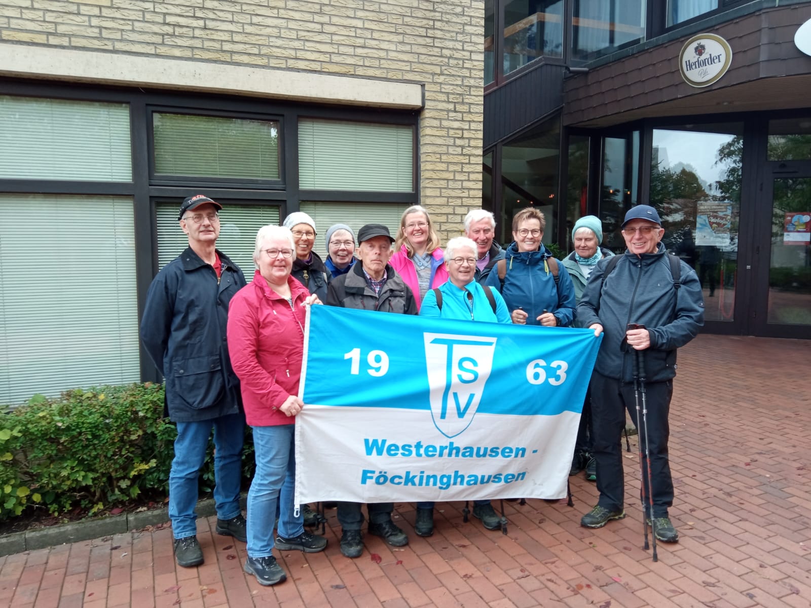 Meller Wandertag 05.10.2025 Gruppe von Personen vor einem Gebäude, die ein blau-weißes Banner mit der Aufschrift 'TSV 1963 Westerhausen-Föckinghausen' hält.