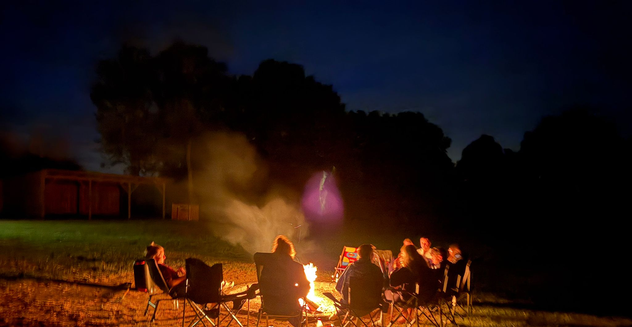Zeltlager Meesdorf 2026 - Tag 4 - Stockbrot Kinder und Jugendliche stehen und sitzen um ein Lagerfeuer und halten lange Stöcke mit Stockbrot über die Flammen